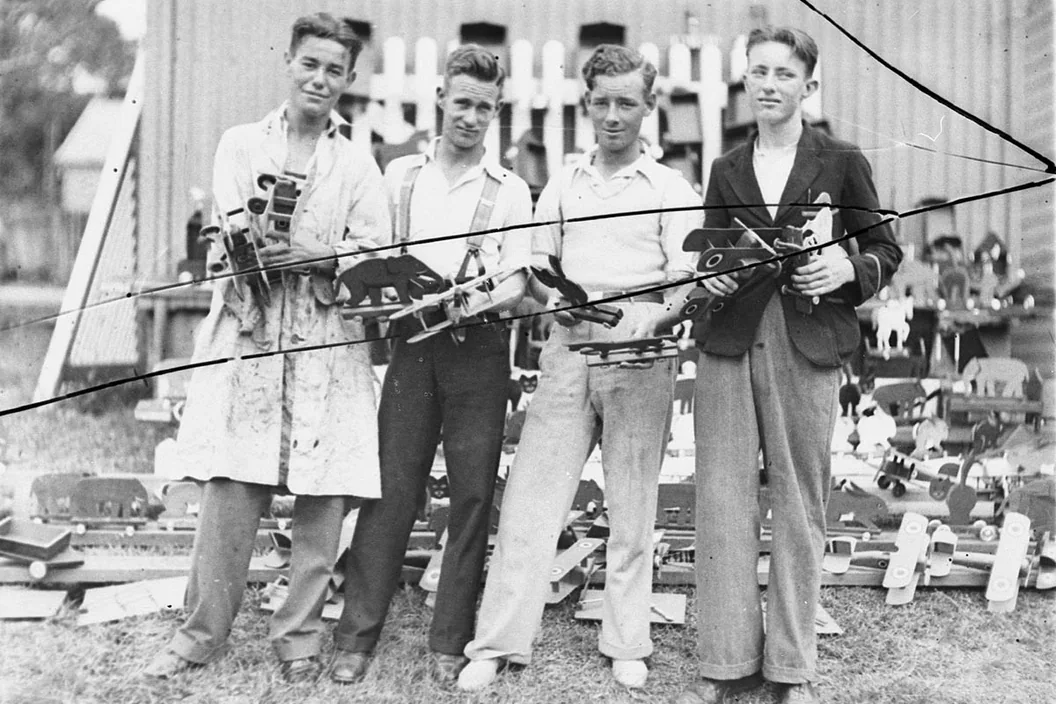 1934 photo of four young men holding wooden toy planes, with long black cracks across it